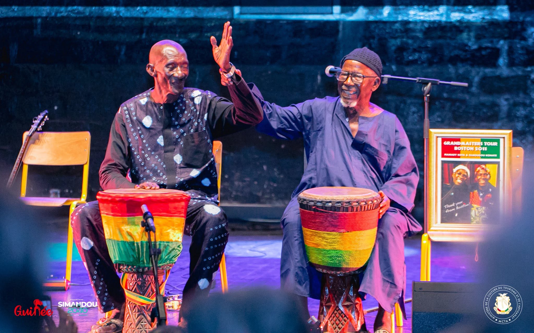 Deux maîtres percussionnistes à leurs djembés lors du lancement officiel du FID, devant le portrait hommage à Mamady Keïta et Famoudou Konaté