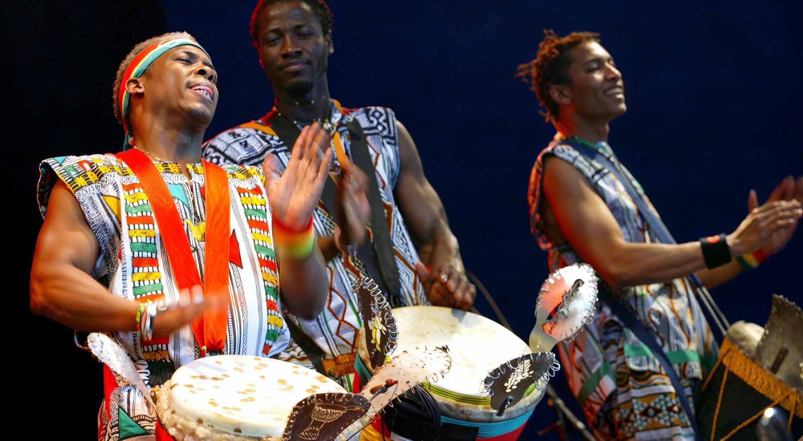 Trois percussionnistes en tenue traditionnelle sur scène, en pleine performance